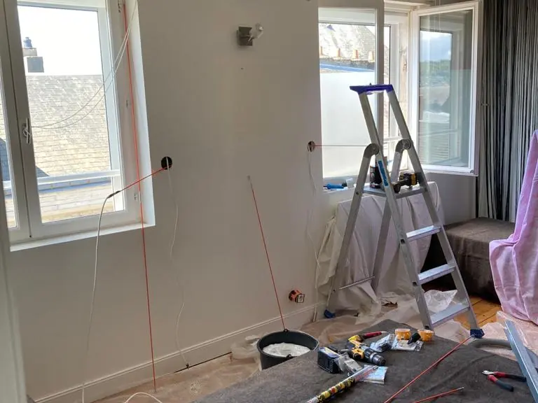 Pièce en travaux avec escabeau et outils devant des fenêtres