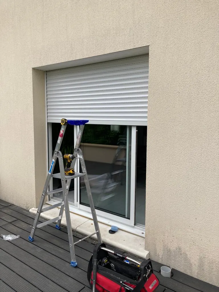Intervention sur un volet roulant depuis une échelle, caisse à outils au pied de la fenêtre